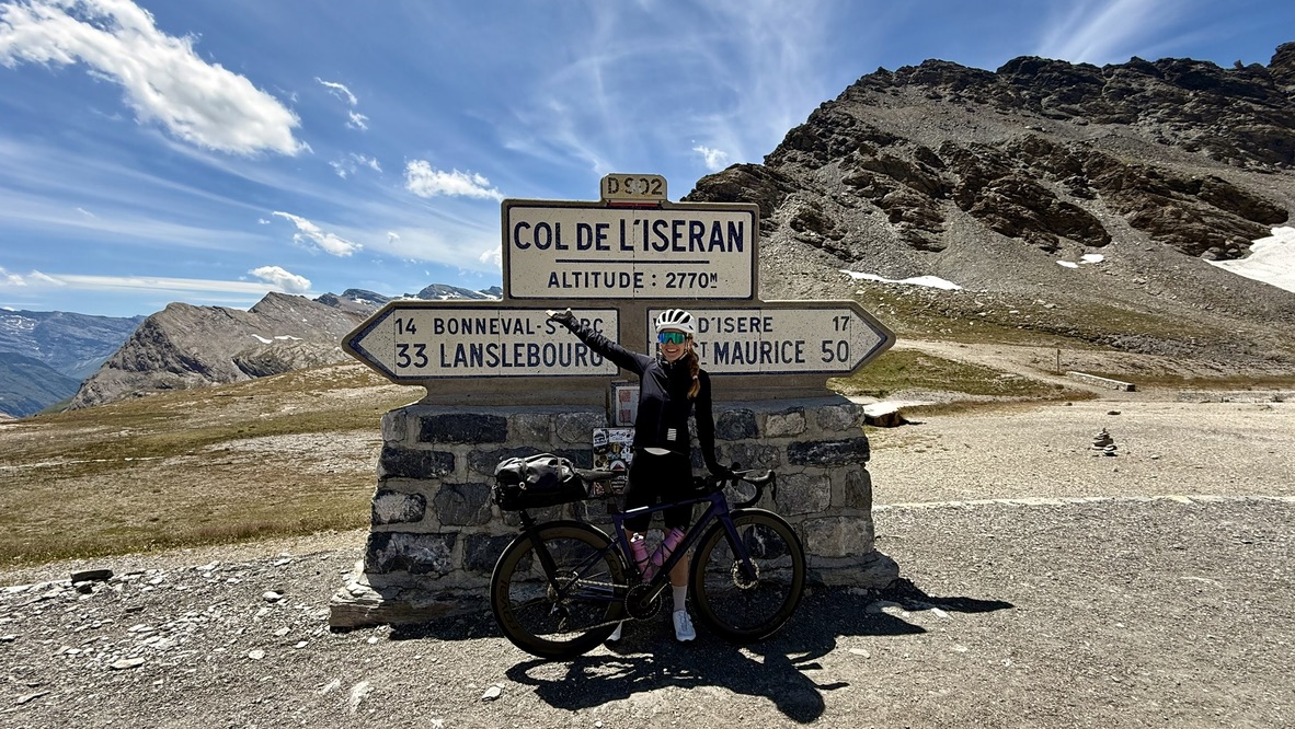 Ramona Furter am Passschild des Col de l'Iseran, neben ihrem Rennrad mit Lenkertasche